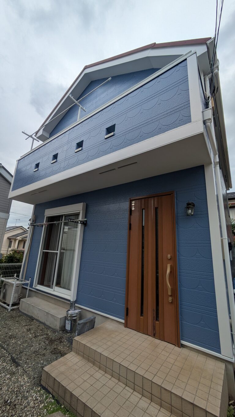 海老名市の戸建て住宅の屋根・外壁リフォーム後の外観。ブルーグレーの外壁に白い縁取りと木目調の玄関ドアが調和した仕上がり。