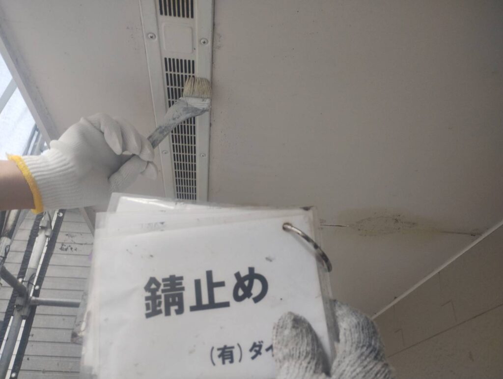 海老名市の住宅の外壁塗装工事で、軒天の換気口に刷毛で錆止め塗料を塗布している様子。